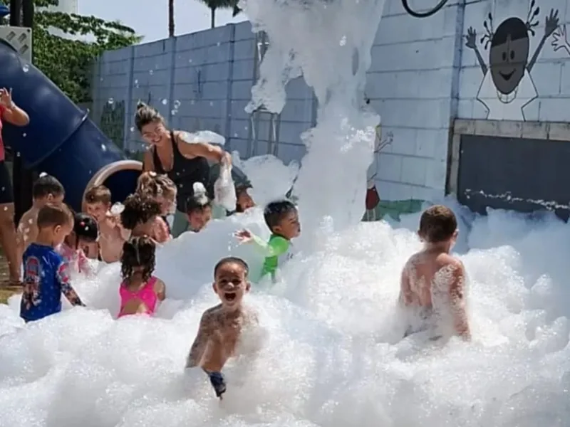 Canhão jogando espuma na festa, com crianças brincando no meio da nuvem
